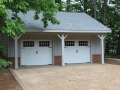 2 car garage with board and batten siding, carriage doors, brick foundation, and paver apron